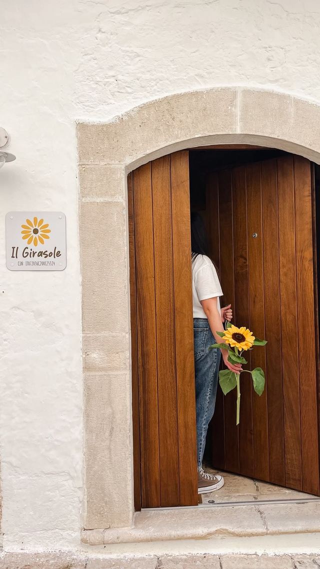 Porta d'ingresso in legno del Girasole con la targa e un'ospite che entra con un girasole in mano