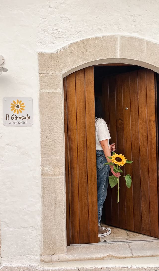 Ingresso in legno della casa vacanze il Girasole nel centro storico di Putignano, con la targa del girasole e un'ospite con un girasole in mano